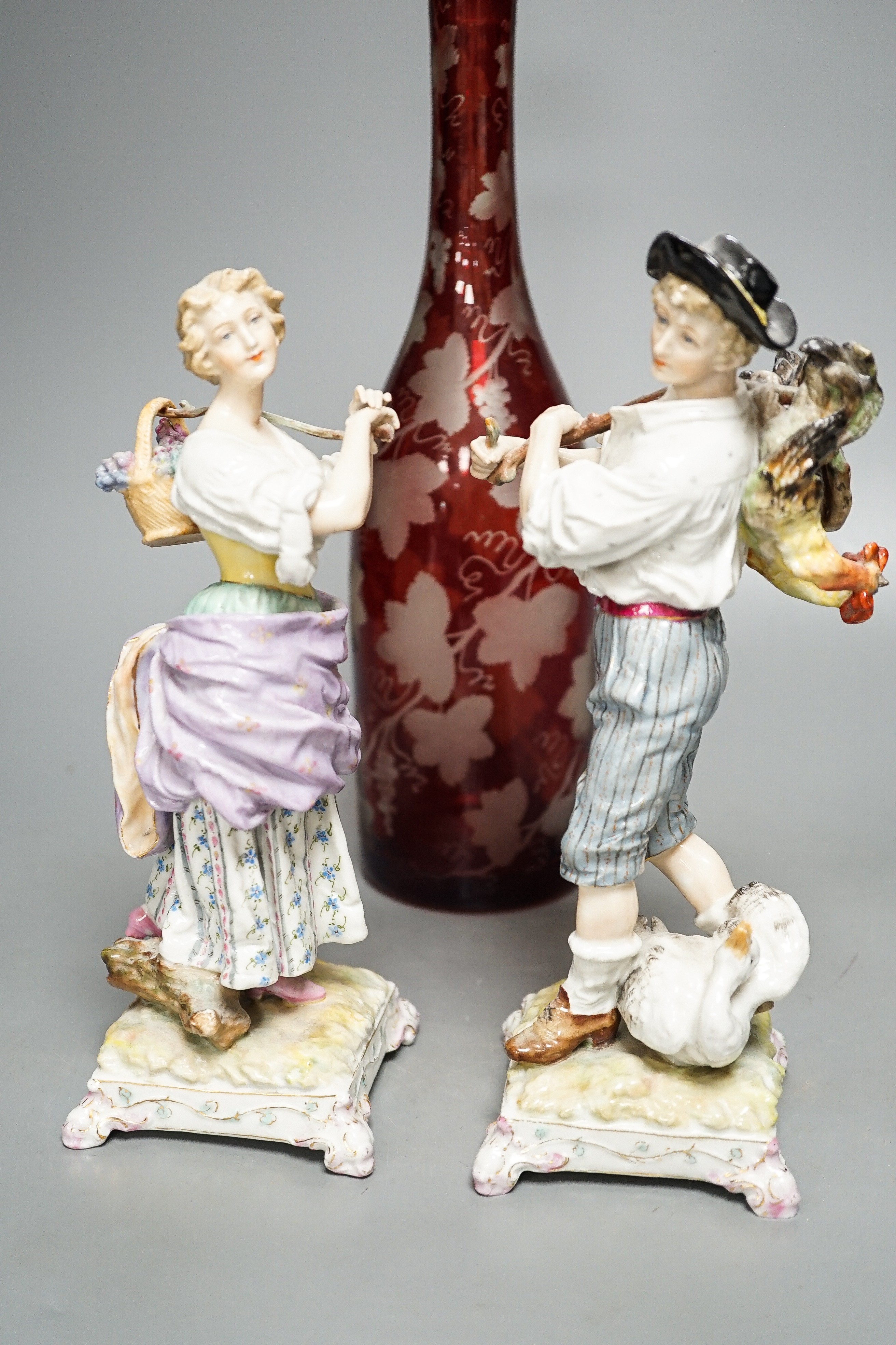 A late 19th century Bohemian wheel engraved ruby glass decanter and a pair of continental porcelain figures, decanter 37 cms high, including stopper.